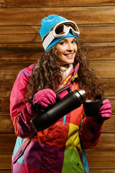 Gelukkige vrouw in ski dragen met thermos tegen houten muur — Stockfoto