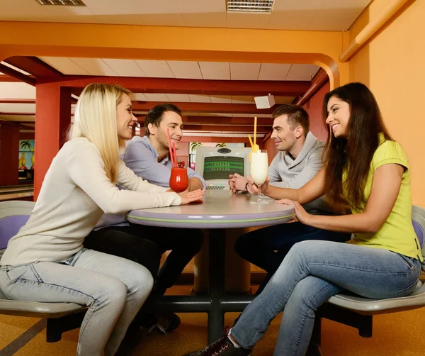 Grupo de cuatro jóvenes sonrientes charlando detrás de la mesa en el club de bolos —  Fotos de Stock