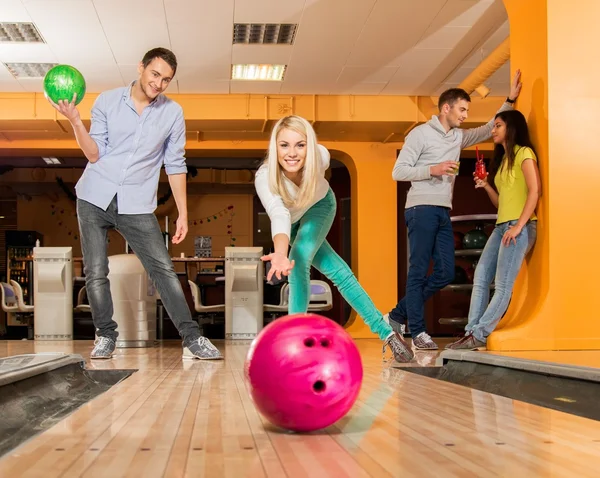 Grupp fyra unga leende människor spelar bowling — Stockfoto