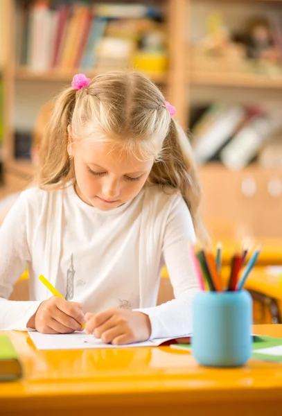 Pequeña colegiala sentada detrás del escritorio escolar durante la lección en la escuela —  Fotos de Stock