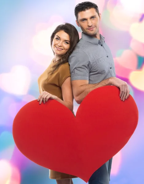 Happy couple in shirt and dress holding handmade paper heart over blurred background — Stock Photo, Image