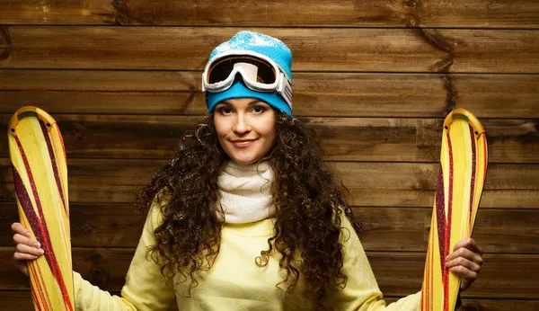 Mujer sonriente con cielos de pie contra la pared de la casa de madera — Zdjęcie stockowe