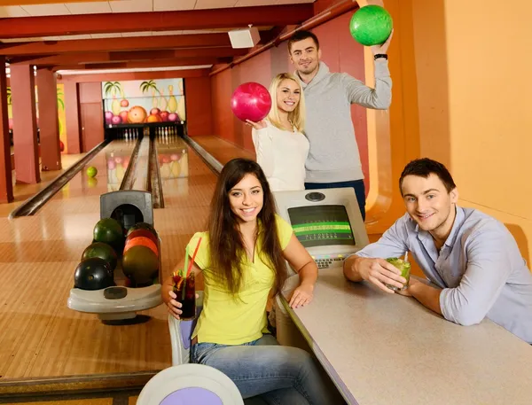 Vier jonge mensen in bowlingclub met ballen en dranken — Stockfoto