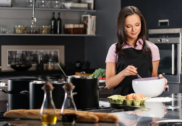 Jonge vrouw in schort eieren voor een deeg te zwaaien op een moderne keuken — Stockfoto