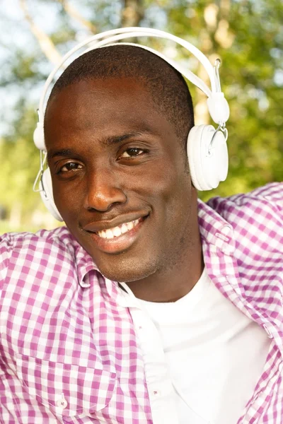 Positive young african american man listens music in a park — Stock Photo, Image