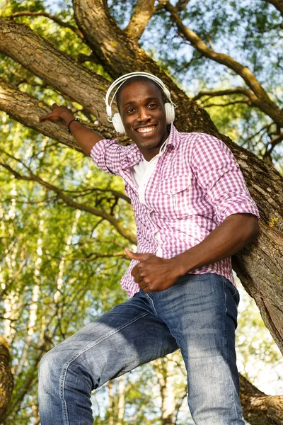 Positive young african american man listens music in a park — Stock Photo, Image