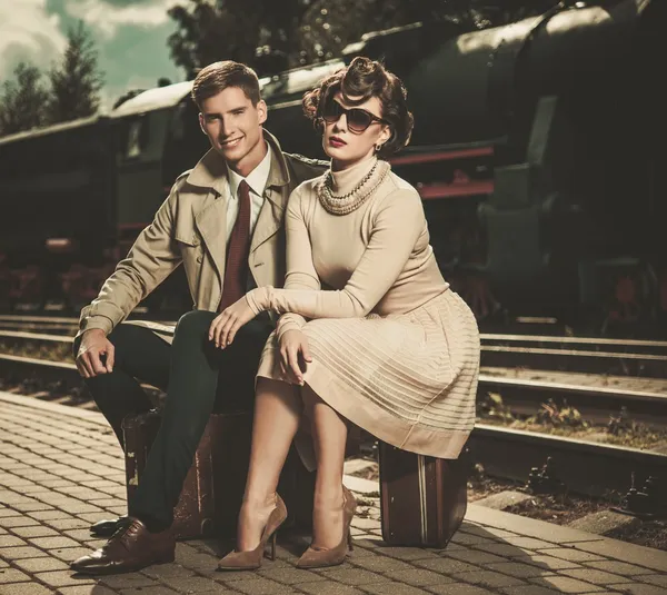 Hermosa pareja de estilo vintage sentada en maletas en la plataforma de la estación de tren — Foto de Stock