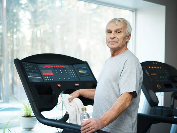 Tired senior man on a treadmill with towel and bottle of water — Stock Photo, Image