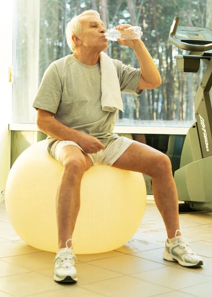 Tired senior man with towel and bottle of water on exercise fitness ball — Stock Photo, Image