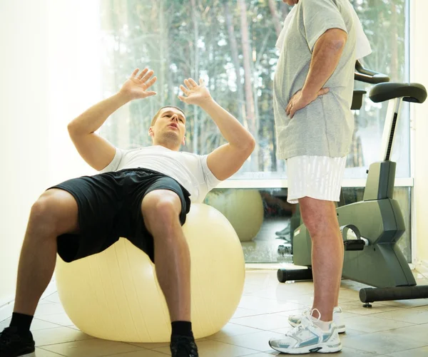 Personlig tränare visar att en äldre man hur man utövar på en fitness boll — Stockfoto