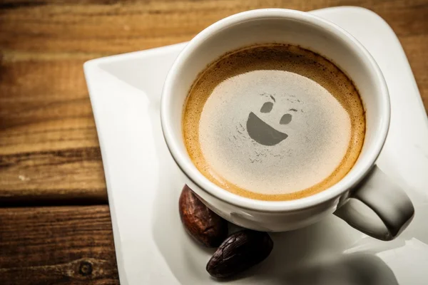 Coffee cup on a wooden table with smiley in it — Stock Photo, Image