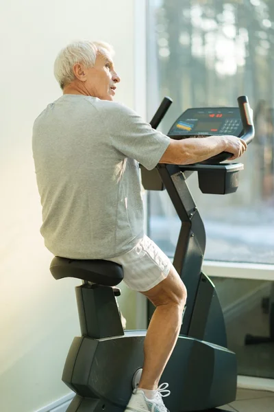 Hombre mayor haciendo ejercicio en una bicicleta en un gimnasio — Foto de Stock