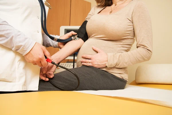 Young pregnant woman in ultrasound examination measuring blood pressure — Stock Photo, Image