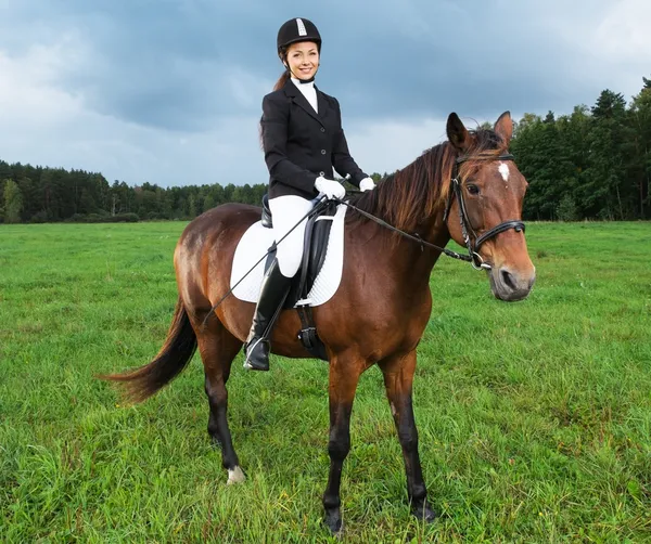 Jovencita alegre montando caballo en un campo —  Fotos de Stock