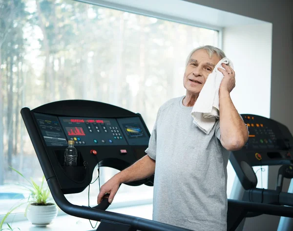 Hombre mayor cansado en una cinta de correr con toalla y botella de agua — Foto de Stock