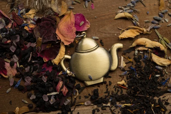 Teapot trinket among flower tea petals on wooden table background — Stock Photo, Image