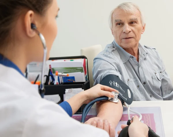 Uomo anziano che misura la pressione sanguigna nello studio del medico — Foto Stock