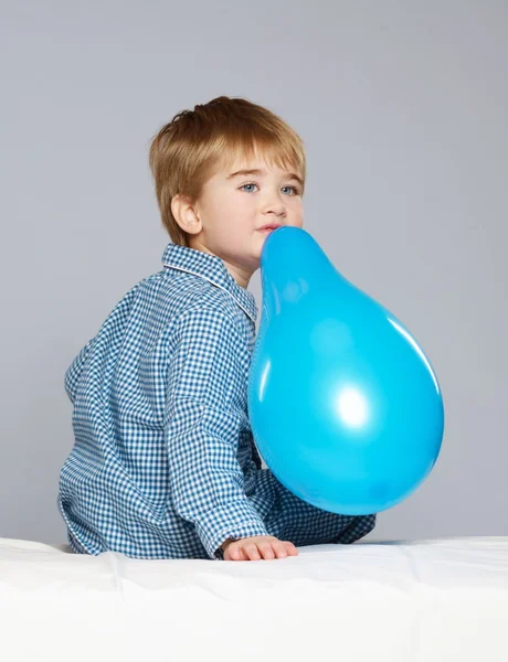 Little boy in blue pyjamas having fun with balloon in bed — Stock Photo, Image