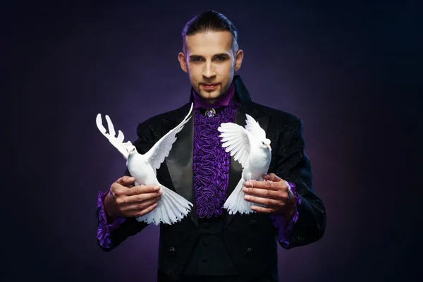 Jovem bonito morena mágico homem no palco traje com seus treinados pombas brancas — Fotografia de Stock