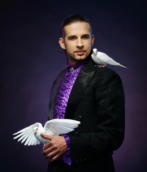 Genç yakışıklı esmer büyücü adam onun eğitimli beyaz güvercinler ile sahne kostüm — Stok fotoğraf