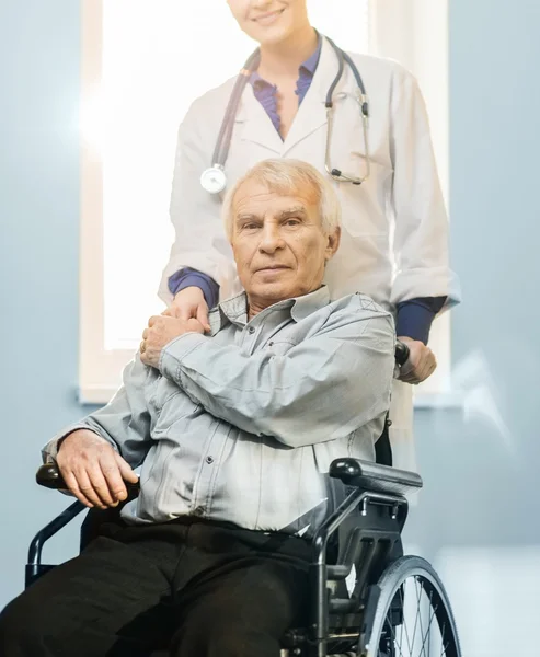 Joven enfermera alegre con hombre mayor en silla de ruedas — Foto de Stock
