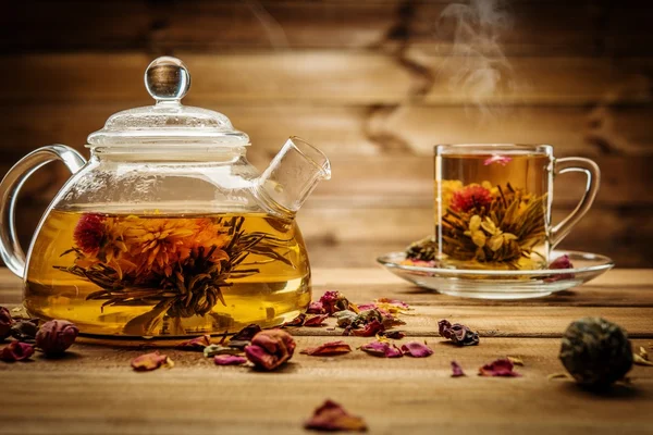 Teapot and glass cup with blooming tea flower inside against wooden background Royalty Free Stock Photos