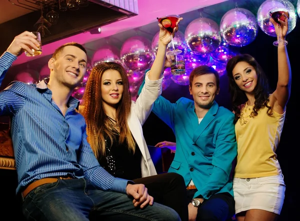 Grupo de jovens amigos alegres sentados com bebidas no clube noturno — Fotografia de Stock