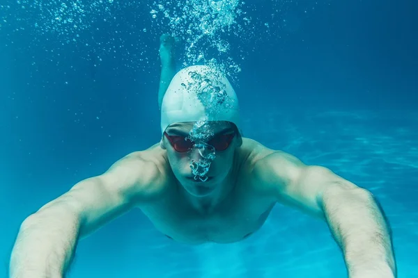 Hombre en gorra de baño y googles bajo el agua en la piscina — Foto de Stock