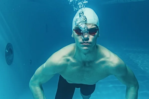 Hombre en gorra de baño y googles bajo el agua en la piscina — Foto de Stock