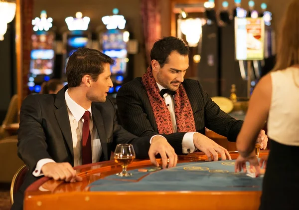 Two young well-dressed men behind gambling table in a casino — Stock Photo, Image