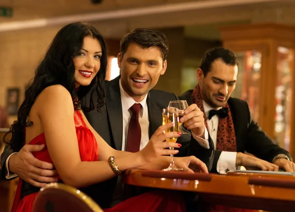 Happy young people behind gambling table with drinks — Stock Photo, Image