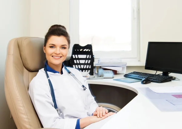 Vrolijke jonge dokter vrouw in haar kantoor achter tafel — Stockfoto