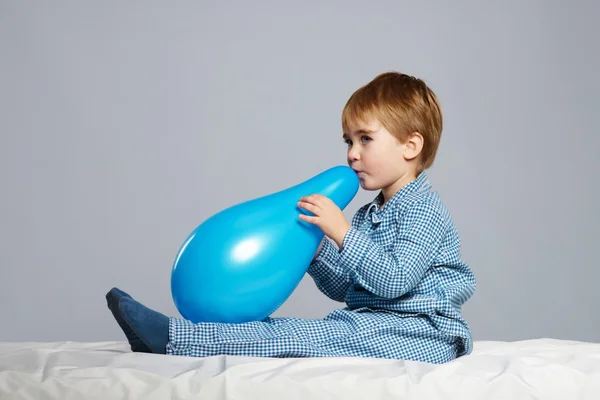 Menino de pijama azul se divertindo com balão na cama — Fotografia de Stock