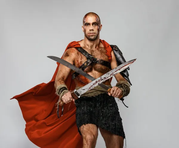 Verwundeter Gladiator mit zwei blutüberströmten Schwertern isoliert auf grau — Stockfoto