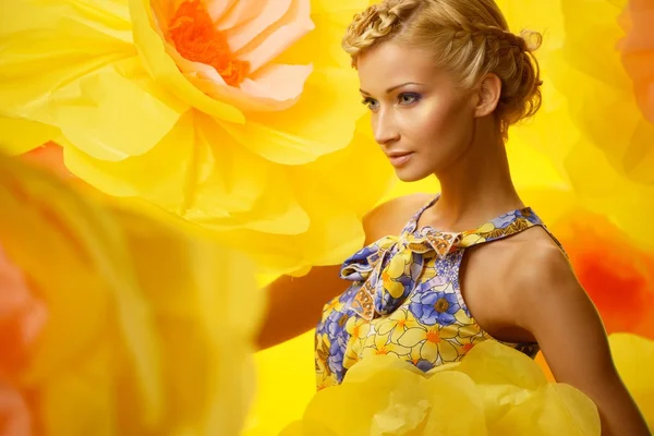 Hermosa joven mujer rubia alegre en vestido colorido entre grandes flores amarillas —  Fotos de Stock