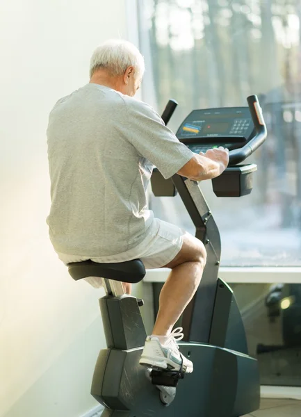 Senior man doing exercise on a bike in a fitness club — Stock Photo, Image