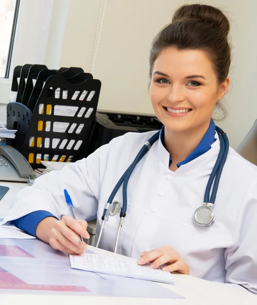 Allegro giovane donna medico nel suo ufficio dietro il tavolo — Foto Stock