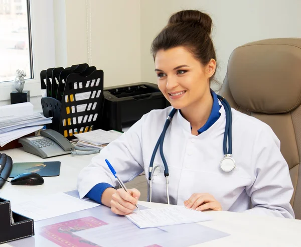 Fröhliche junge Ärztin in ihrem Büro hinter dem Tisch — Stockfoto