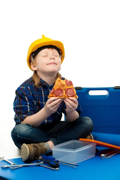 Little funny mechanic boy eating pizza among tools — Stock Photo, Image