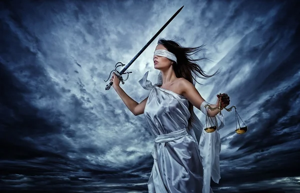Фемида, Богиня Справедливости, с чешуей и мечом в повязке на глазах на фоне бурного неба — стоковое фото