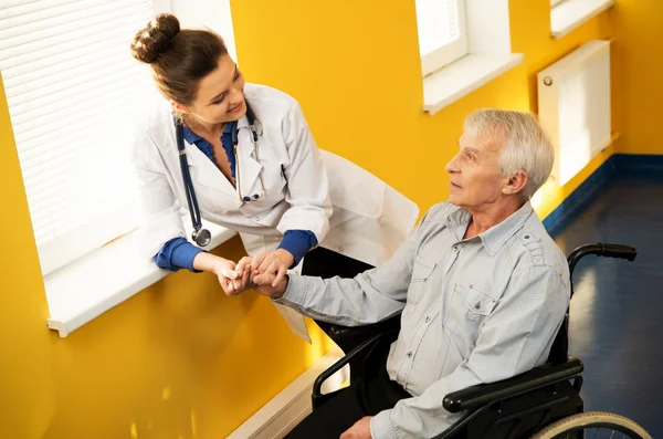 Fröhliche junge Krankenschwester mit älterem Mann im Rollstuhl — Stockfoto