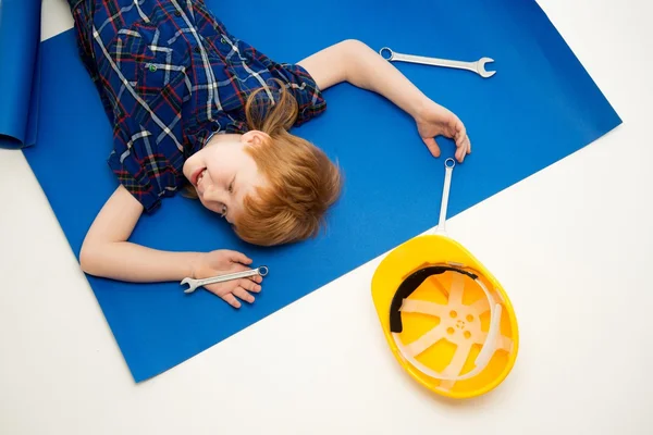 Funny little mechanic boy with wrench tools lying on a blueprint — Stock Photo, Image