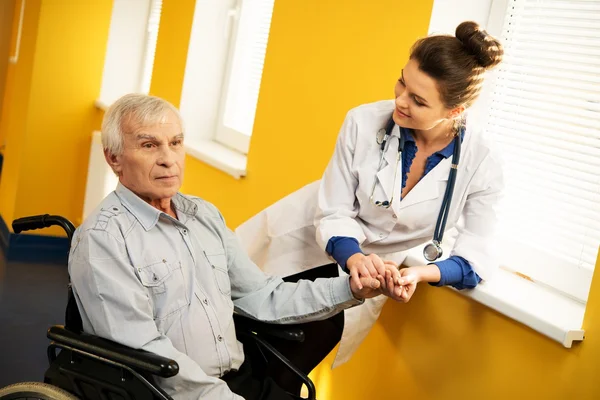 Fröhliche junge Krankenschwester mit älterem Mann im Rollstuhl — Stockfoto