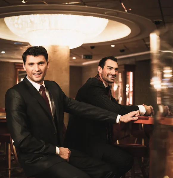 Two young men in suits behind gambling table in a casino — Stock Photo, Image