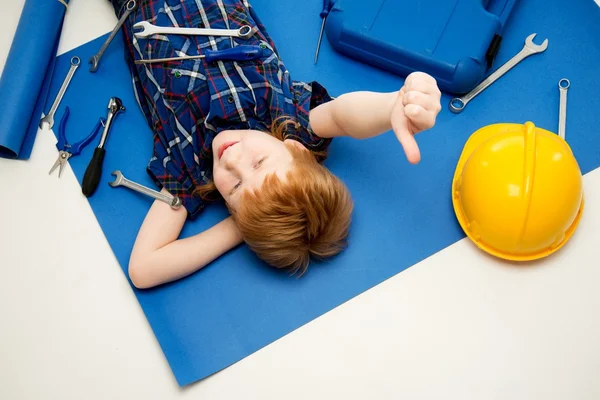 Lustiger kleiner mechanischer Junge mit Schraubenschlüssel, der auf einem Bauplan liegt — Stockfoto