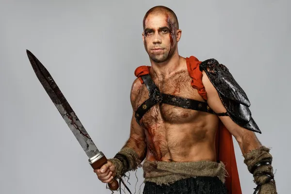 Gladiador ferido com espada coberta de sangue isolado em cinzento — Fotografia de Stock