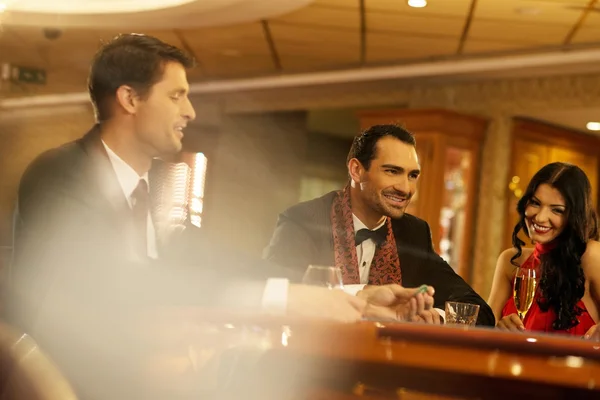 Happy young people behind gambling table with drinks — Stock Photo, Image