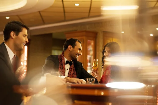 Happy young people behind gambling table with drinks — Stock Photo, Image