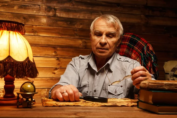 Seniorchef mit Lupe betrachtet alte Landkarte im gemütlichen Holzinterieur — Stockfoto