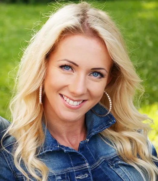 Beautiful young blond woman in a blue jacket sitting on a bench in a park — Stock Photo, Image